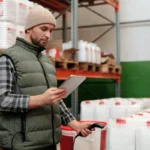 Staf gudang mengelola inventori dengan tablet di rak penyimpanan barang